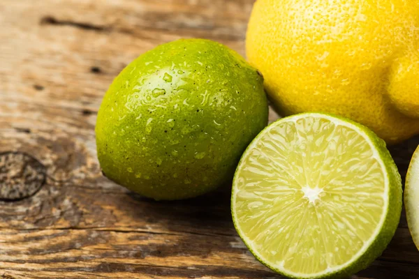 Limones y lima frescos y jugosos sobre una superficie de madera — Foto de Stock