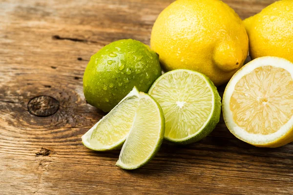 Limões e limão frescos e suculentos em uma superfície de madeira — Fotografia de Stock