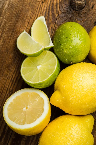 Limões e limão frescos e suculentos em uma superfície de madeira — Fotografia de Stock