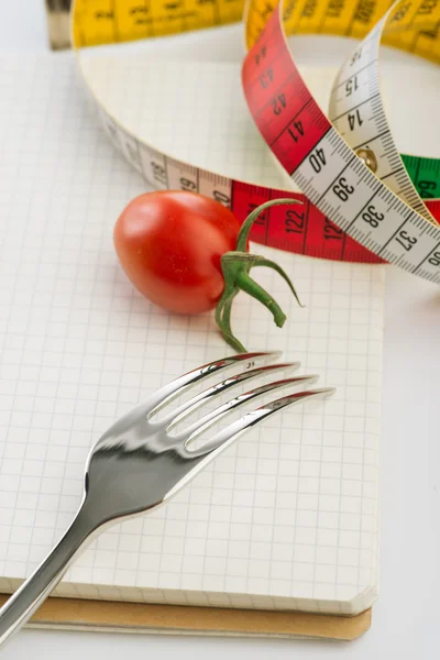 Tenedor, bloc de notas, cinta métrica y tomate sobre el fondo blanco — Foto de Stock