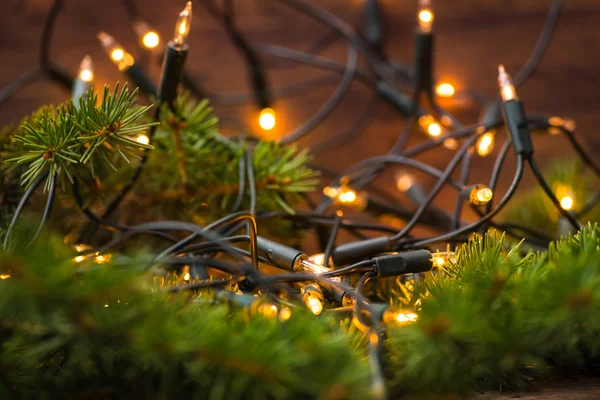 Rama de abeto con luces navideñas sobre la superficie de madera — Foto de Stock