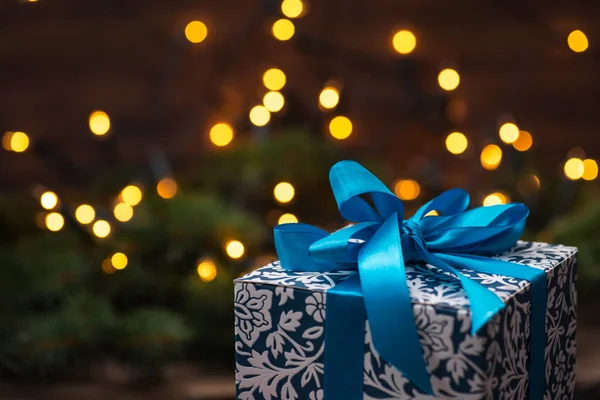 Caja de regalo de Navidad con lazo azul y luces en la superficie de madera — Foto de Stock