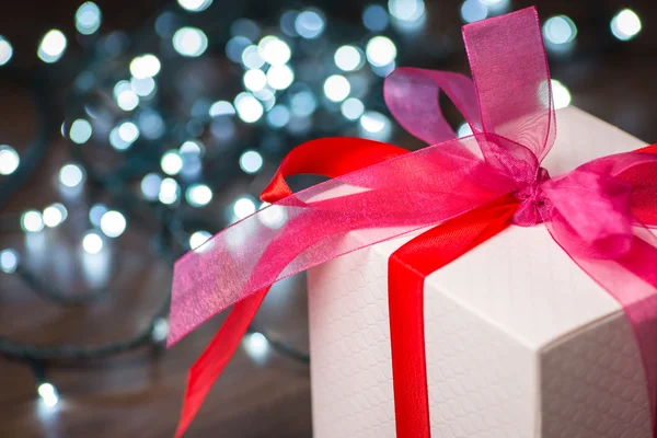 Caja de regalo de Navidad con lazo rojo y luces en la superficie de madera — Foto de Stock