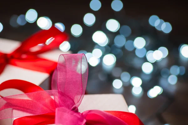 Cajas de regalo de Navidad con lazo rojo y luces en superficie de madera — Foto de Stock