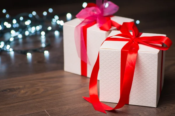 Caixas de presente de Natal com arco vermelho e luzes na superfície de madeira — Fotografia de Stock