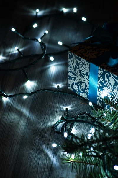 Caja de regalo de Navidad con lazo azul y luces en la superficie de madera — Foto de Stock