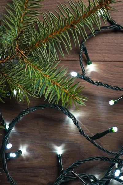Rama de abeto con luces navideñas sobre la superficie de madera — Foto de Stock