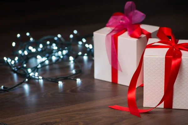 Cajas de regalo de Navidad con lazo rojo y luces en superficie de madera — Foto de Stock