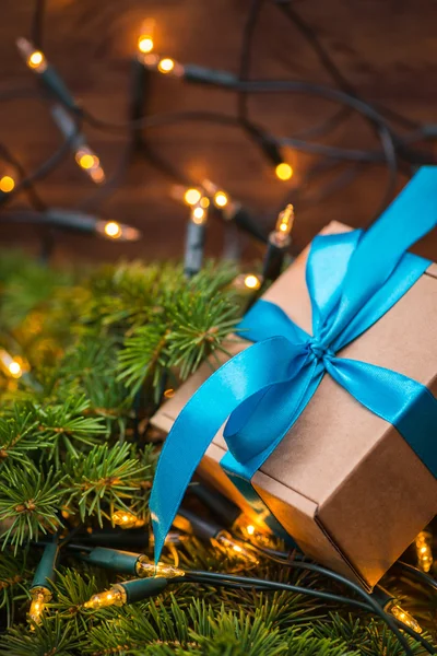 Caja de regalo de Navidad con lazo azul y luces en una rama de abeto — Foto de Stock