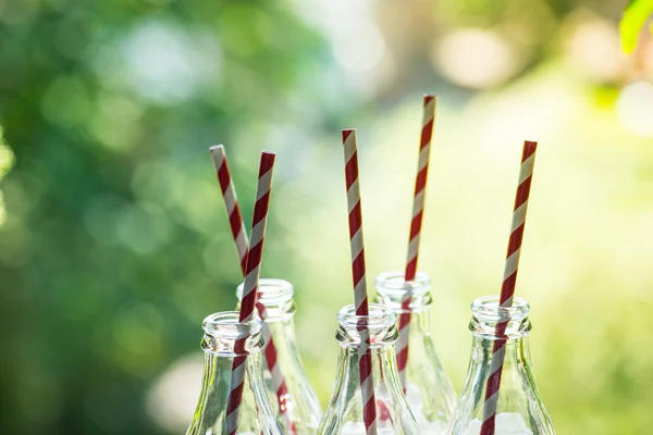 Glazen flessen met rietjes op de zonnige achtergrond — Stockfoto