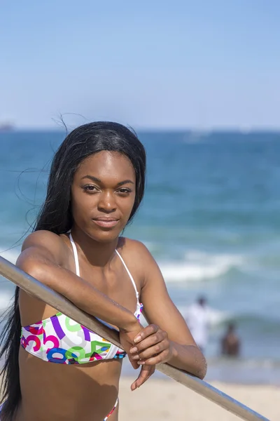 Giovane donna nera in spiaggia, in bikini. Appoggiato sulla ringhiera. Cielo blu . — Foto Stock