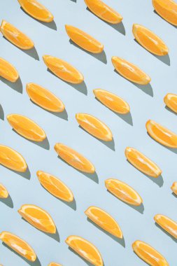 Pastel mavi arka planda taze portakal dilimleriyle yaratılmış yaratıcı desen. Minimum güneş ışığı düzlüğü.