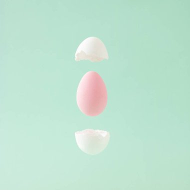 Pastel yeşil arka planda yumurta kabuğunun arasında uçuşan paskalya pembe yumurtası. Asgari konsept.