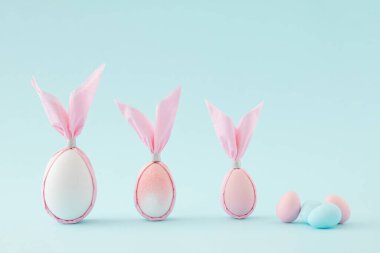 Pastel mavi arka planda tavşan şeklinde paskalya pembesi ve beyaz yumurtalar. En düşük bileşim.