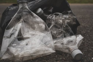 Siyah çöp torbası ezilmiş plastik şişelerle dolu bir sokakta