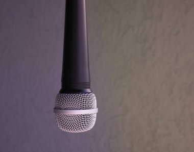 asılmış mikrofon. Metal kapaklı mikrofonun neredeyse tamamını görebilirsiniz. Arkanızda gri bir duvar görebilirsiniz.