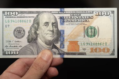 Yüz dolarlık banknotu tutan el. Önden gözlemlendi. Faturanın yüzünü görebilirsin..