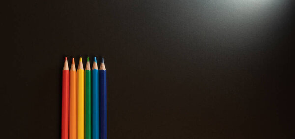 some colors pencils on a black background with copy space. the colors representative the colors of the gay pride flag.