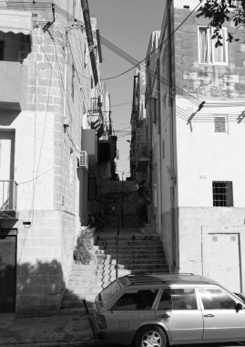Tarihi Malta kasabasında siyah ve beyaz dar bir ara sokak, kireçtaşı binalar arasında dik taş merdivenler, tepetaklak kablolar, çamaşırhane, park edilmiş araba, otantik Akdeniz eski çeyreği