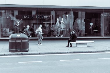 Sokak fotoğrafçısı, oturan kadın almak insanlar tonlama bölünmüş Londra'da, siyah ve beyaz fotoğraf, Oxford Caddesi'nde yürüyen bir fotoğraf