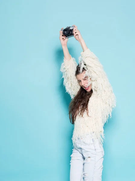 Модная стильная женщина танцует и делает фото с помощью ретро-камеры. Портрет на синем фоне в белом свитере — стоковое фото