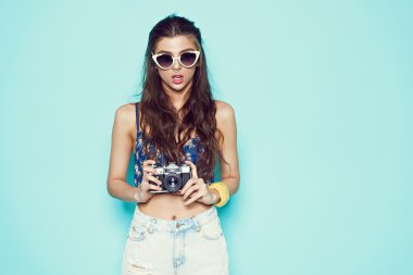 moda şık kadın sungalasses Retro kamera ile fotoğraf yapma. Portre beyaz kazaklı mavi arka plan üzerinde