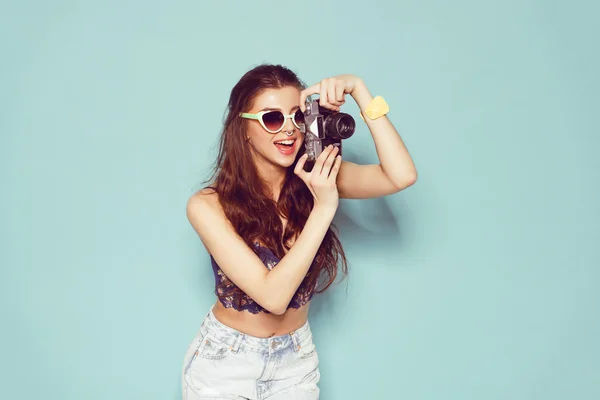 Mode stijlvolle vrouw dansen en het maken van foto met behulp van retro camera. Portret op blauwe achtergrond in witte trui — Stockfoto