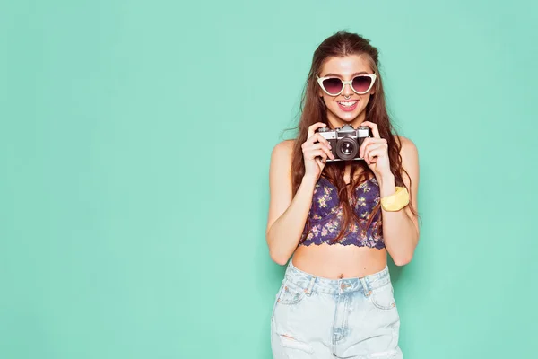 Mode stijlvolle vrouw dansen en het maken van foto met behulp van retro camera. Portret op blauwe achtergrond in witte trui — Stockfoto