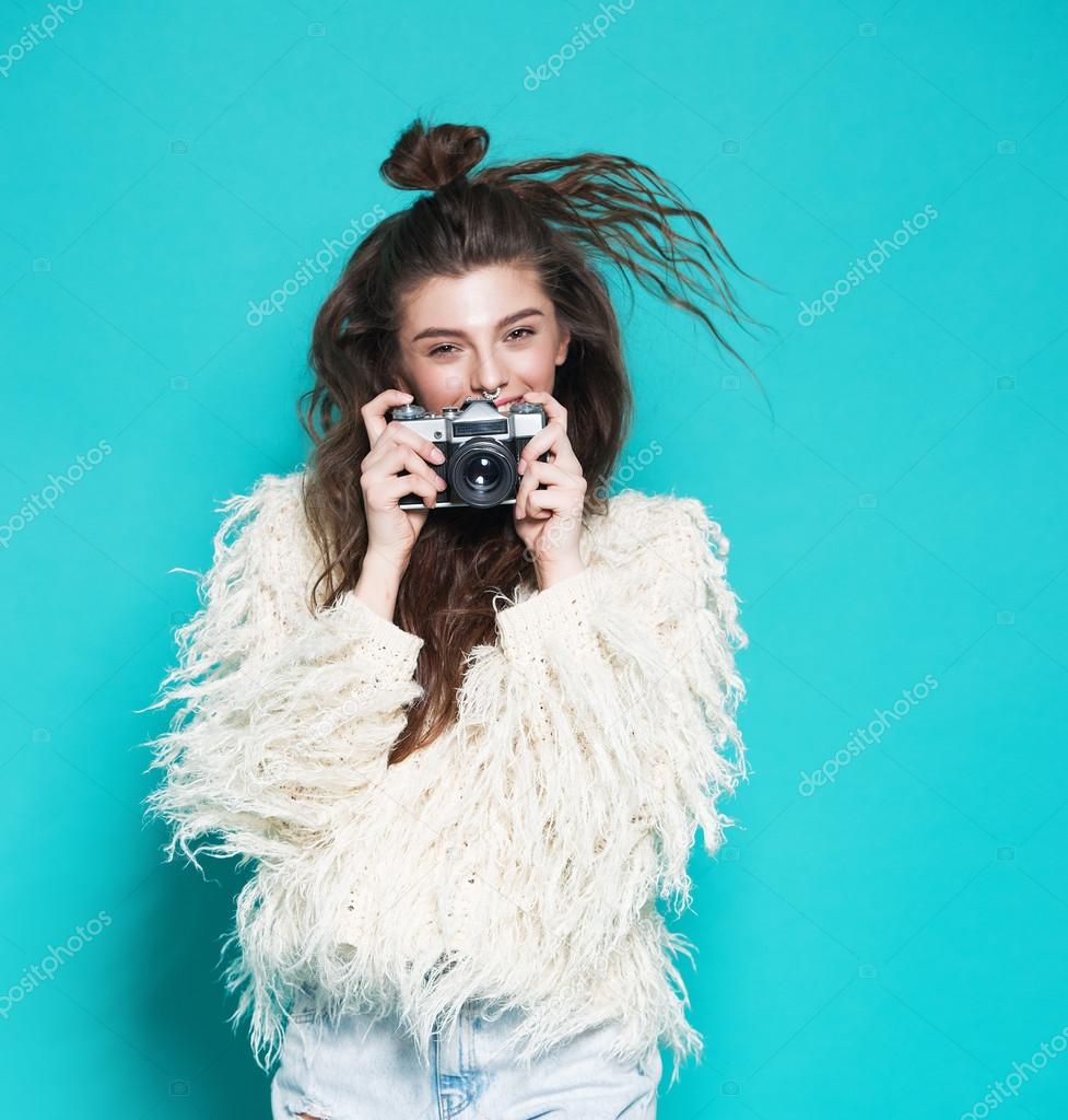 fashion stylish woman dancing and making photo using retro camera. Portrait on blue background in white sweater