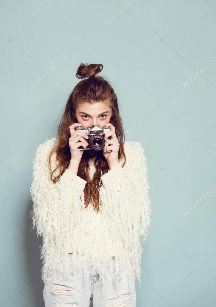 fashion stylish woman dancing and making photo using retro camera. Portrait on blue background in white sweater