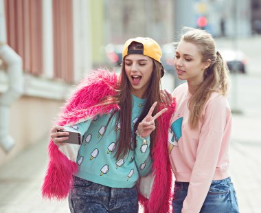 Hipster girlfriends taking a selfie in urban city context - Concept of friendship and fun with new trends and technology - Best friends eternalizing the moment with modern smartphone clipart