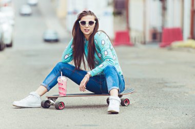 güzel bir genç kadın bir kaykay, gün batımında moda yaşam tarzı ile poz