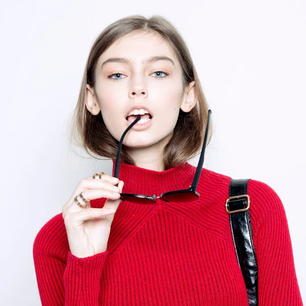 Portrait de fille de mode dans un chandail rouge élégant et des lunettes de soleil sur un fond blanc. Style urbain — Photo