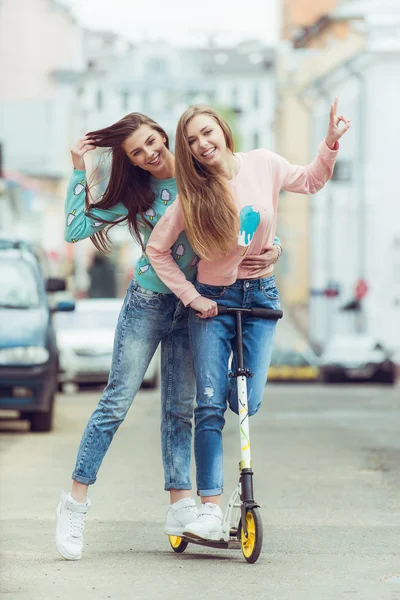 Color fashion portrait of beautiful glam street style girlfriends standing near grange wall. keep cocktail in a hand — Stock Photo, Image