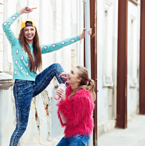 Цветной модный портрет красивых девушек глэм-стрит, стоящих рядом с гранж-стеной. Держать коктейль в руке — стоковое фото