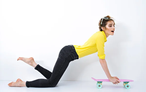 Mode hipster meisje in gele overhemd in zonnebril met skateboard flirten tegen de witte muur — Stockfoto