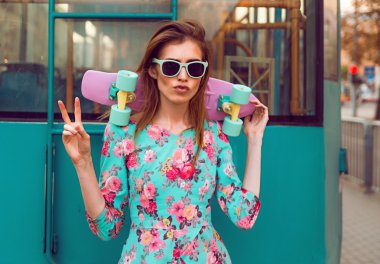 Beautiful and fashion young woman posing with a skateboard on city street clipart