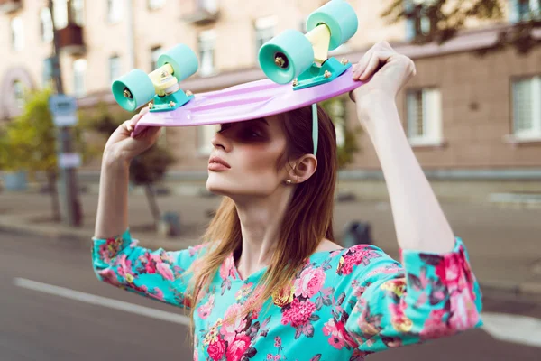 Beautiful and fashion young woman posing with a skateboard on city street — Stock Photo, Image