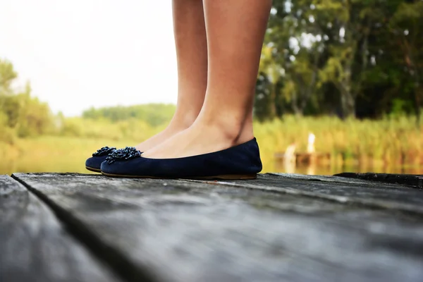 De benen van de vrouw in modieuze schoenen staande op een houten dek — Stockfoto