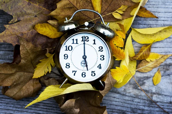 Retro clock on a wooden table with autumn leaves Royalty Free Stock Images
