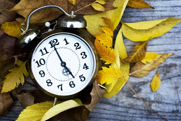 Retro clock on a wooden table with autumn leaves Royalty Free Stock Images
