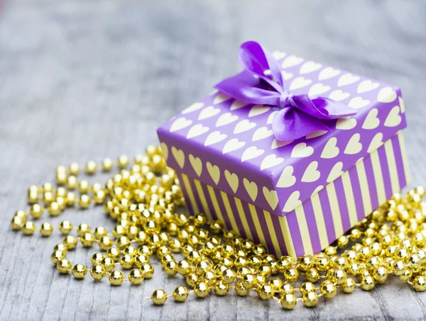 กล่องของขวัญสีม่วงที่มีหัวใจสีเหลืองบนไข่มุกสีทอง — ภาพถ่ายสต็อก