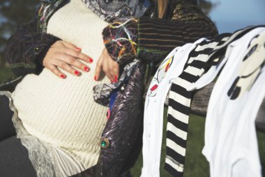 Bebek giysileri ile bir bankta oturan hamile kadın