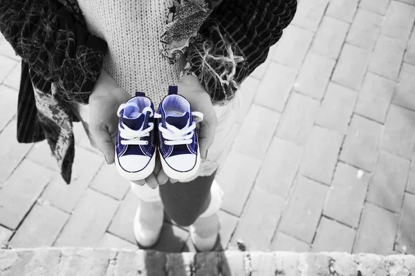 Schwangere steht und hält blaue Babyschuhe — Stockfoto