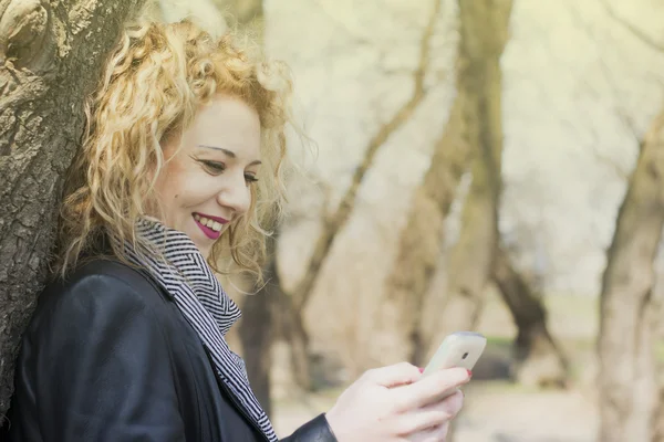 Mladá kudrnatá blondýna psaní na telefonu v přírodě — Stock fotografie