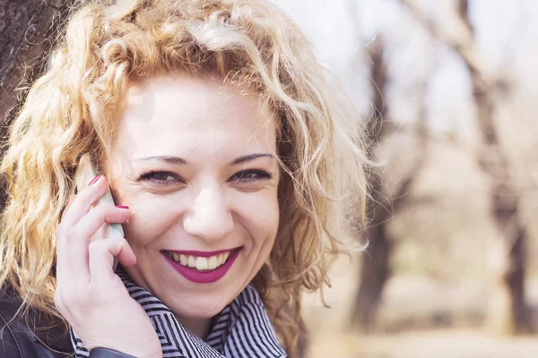 Young curly blond woman talking on the phone in outdoors — Stock Photo, Image