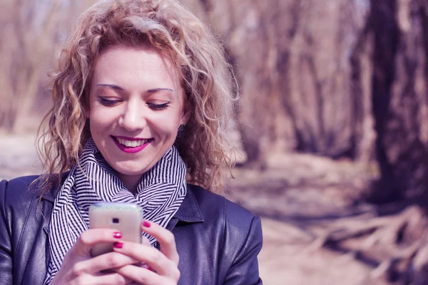 Mladá kudrnatá blondýna psaní na telefonu v přírodě — Stock fotografie