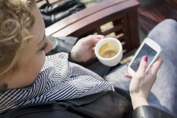 Mladá kudrnatá blondýnka pití kávy a psaní na telefonu — Stock fotografie