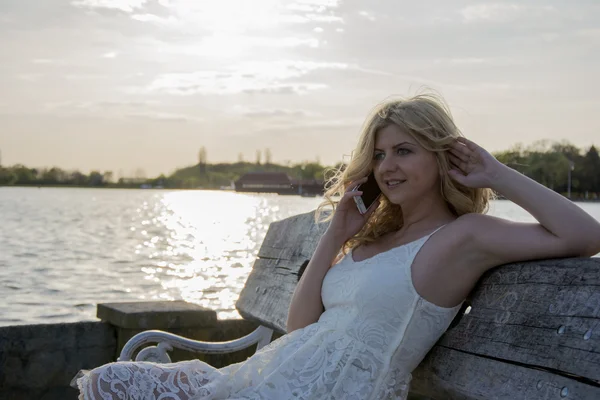 Blond kobieta rozmawia przez telefon nad jeziorem — Zdjęcie stockowe