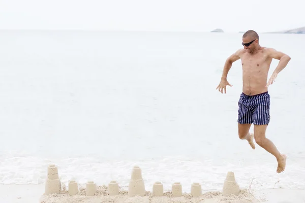 Man springen op strand boven zandkasteel — Stockfoto